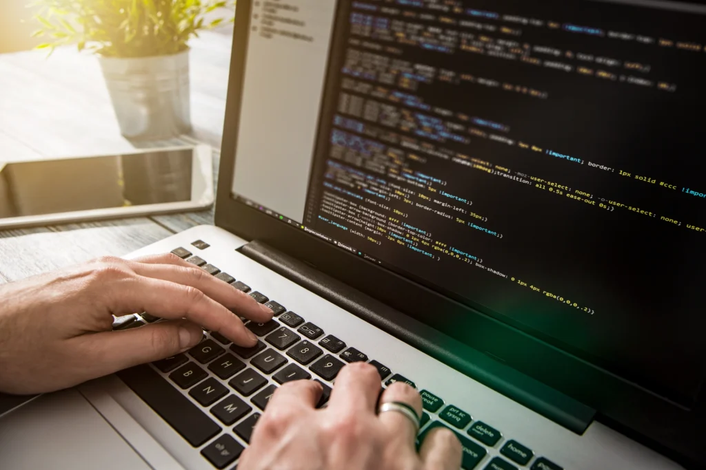Osoba pisze kod na laptopie, na ekranie widoczny edytor z programowaniem.