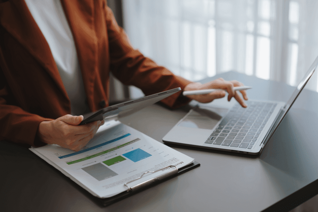 Osoba analizuje wykresy na tablecie, korzystając z laptopa przy biurku.