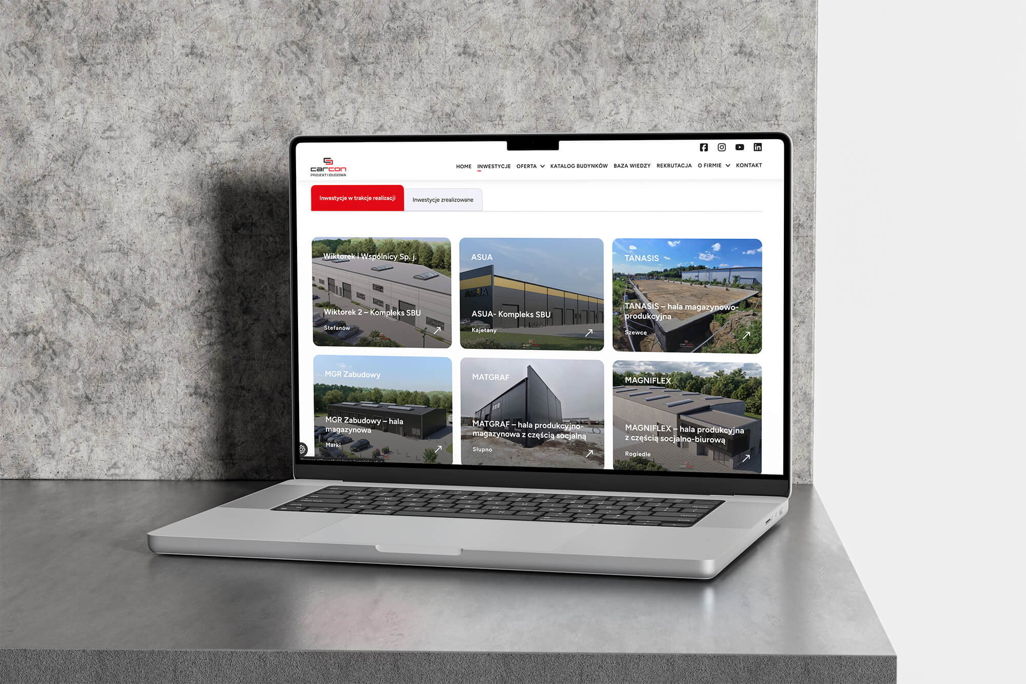 Laptop z otwartą stroną internetową z galerią realizacji budynków i hal produkcyjnych.